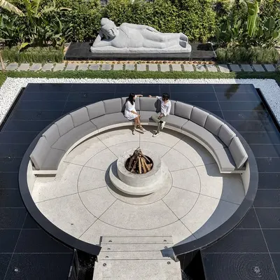 An aerial day view reveals the perfect geometry of this outdoor sanctuary. The circular sunken lounge with its central fire pit is perfectly centered within a square water body, creating a powerful sense of balance and order. The design provides a space for connection, surrounded by water and greenery.