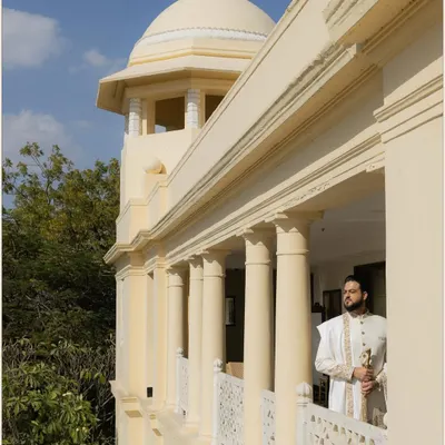 A regal portrait of the groom standing on a palace balcony, looking out thoughtfully. The architecture and natural light create a majestic and timeless feel.