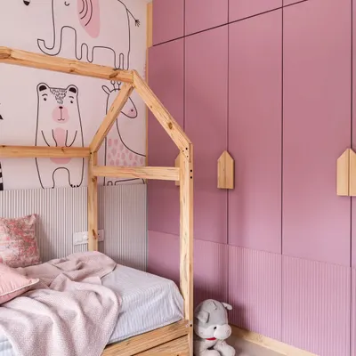 For this shared girls' bedroom, the main request was a pink color scheme and ample storage. To solve the challenge of a compact space, I used a trundle bed that folds away, making room for a study area. The house-frame bed and animal-themed wallpaper add a playful touch.