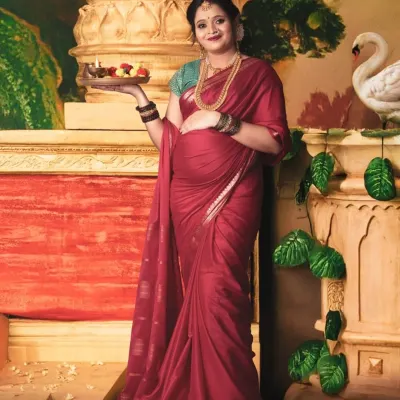 A vision of traditional grace. This mom-to-be, dressed in a beautiful red saree and holding a puja thali, is captured in a setting that evokes the feeling of a classic Indian painting.