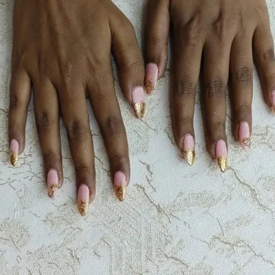 An elegant set of gel nail extensions. We created this look with a soft pink base and added a touch of glamour with gold glitter tips and subtle stone work, perfect for a special occasion.