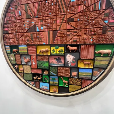 A detailed shot of a mixed-media piece. This circular work combines geometric wood carving with miniature painted scenes, exploring the tension between urban structures and the natural world.