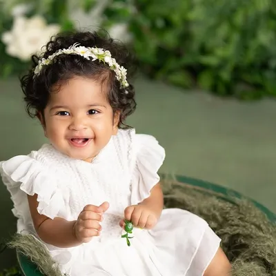 A beautiful sitter session portrait with a lush green backdrop. Her bright, happy smile and the simple white dress make this a timeless and classic baby photo.