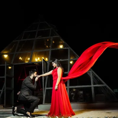 A dramatic pre-wedding photo at night. The groom's proposal pose, the bride's flowing red dress, and the unique pyramid location create a truly cinematic and memorable shot.