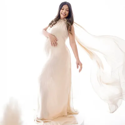 A moment of pure joy and elegance. This mama-to-be is captured in a flowing cream gown against a high-key white background, creating a light and ethereal portrait.