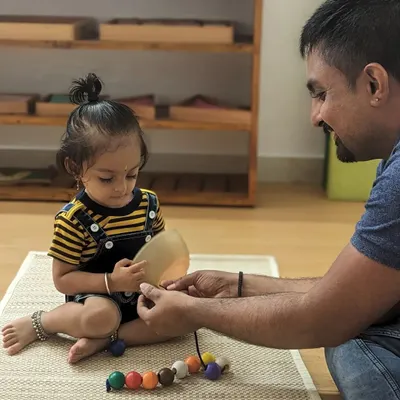 A father guides his daughter in a beading activity, a simple joy that helps develop fine motor skills and concentration. These one-on-one moments are precious parts of the learning process.