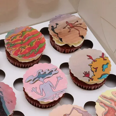 A detailed look at the edible art toppers, based on original drawings by the artist @ool_jalool. Each cupcake features a different abstract figure, printed on an edible sheet and placed on a red velvet base.