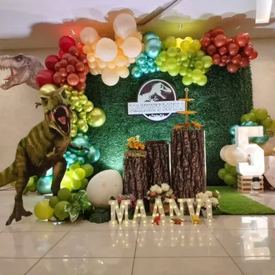 A thrilling Jurassic World theme with a large T-Rex prop, a grass wall backdrop, and tree stump pedestals.