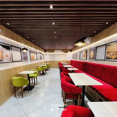 This cafe interior features a bold and inviting color scheme. The contrast between the plush red velvet booths and the vibrant lime green chairs creates a lively atmosphere, while the linear layout ensures a smooth flow for customers and staff.