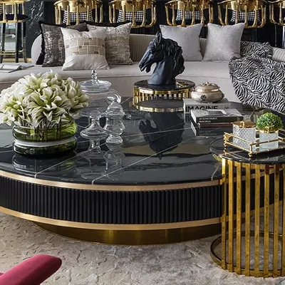 A close-up of a custom-designed living room set. The fluted black base of the coffee table, topped with black marble, contrasts with the gold-caged side table and the plush, neutral-toned sofa.