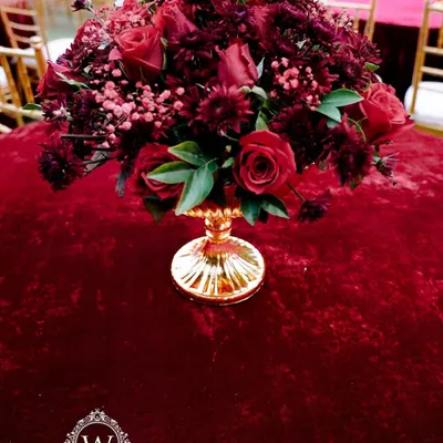 A luxurious centerpiece featuring a bouquet of deep red roses in a golden vase. This classic and elegant detail was part of a glamorous red-themed reception.