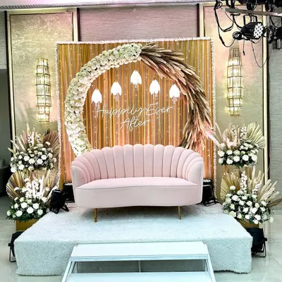 A beautiful seating area for the couple to begin their "Happily Ever After." This boho-chic setup features a pampas grass and floral crescent, a neon sign, and a lovely pink sofa.