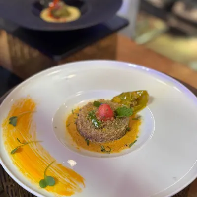 A minimalist canvas for maximum taste. This dish features a quinoa base with a vibrant sauce, garnished with microgreens and pickled chili, showcasing our belief that food should be both beautiful and delicious.
