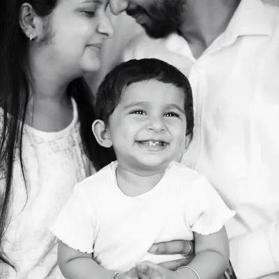 A joyful black and white family portrait, with the baby's bright smile at the center of his parents' loving gaze.
