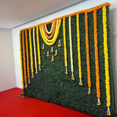 A versatile greenery wall backdrop. This simple yet elegant design is decorated with hanging garlands of yellow, orange, and white flowers, suitable for any festive occasion.