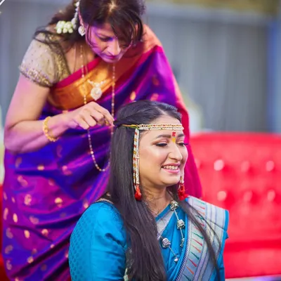 A sweet, candid moment of a mother helping her daughter with her hair and jewelry before a ceremony. These quiet, intergenerational moments are priceless memories.