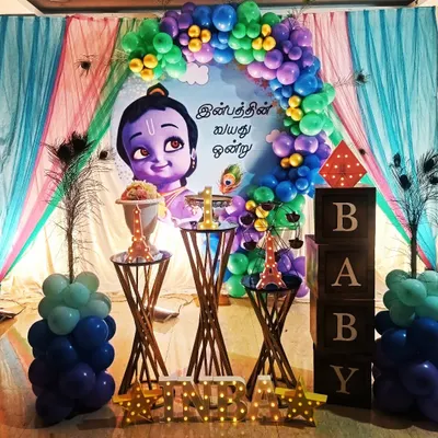A beautiful and traditional theme featuring Little Krishna for a first birthday. The decor uses peacock feathers and a vibrant color palette to create a divine and celebratory atmosphere.