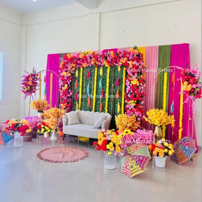 A grand and colorful Mehendi setup, featuring a vibrant floral frame, a green wall with tassels, and an abundance of bright flowers. This decor is perfect for making a statement.