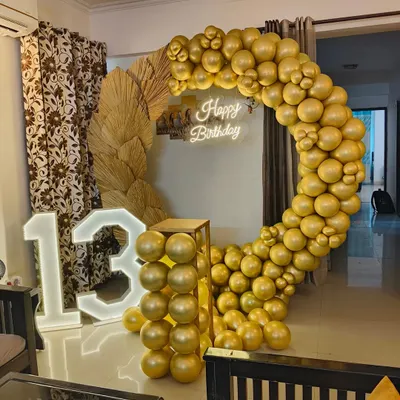 A stylish and modern setup for a 13th birthday party. This decoration features a large marquee number '13', a circular balloon arch in metallic gold, and dried pampas grass for a trendy, bohemian touch.