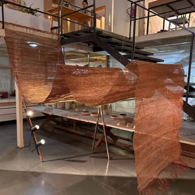 A free-flowing woven sculpture from our 'Cu+Fibers' exhibition, created in our studio. This piece is a play of hand-spun and machine-made fibers like hemp, jute, and copper, manipulated and formed to catch the light.