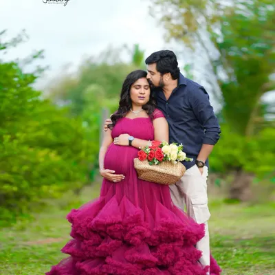 An intimate outdoor moment with the couple dressed in a stunning magenta gown. The natural greenery and the tender kiss create a romantic and unforgettable portrait.