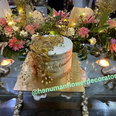 I can help you create a complete celebration centerpiece. This setup for a special birthday features a beautiful cake surrounded by a custom arrangement of fresh lilies, carnations, and baby's breath, accented with warm fairy lights.