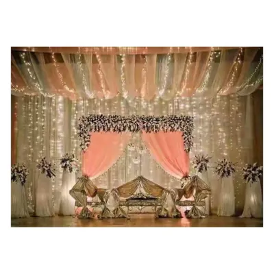 A classic reception stage featuring a beautiful floral arch, delicate pink draping, and a backdrop of twinkling fairy lights. This design creates a romantic and elegant focal point for any wedding or mehendi ceremony.
