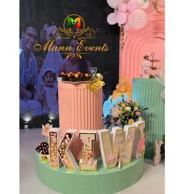 A close-up of a pastel-themed dessert table, featuring personalized 'KIWI' letters, a neon butterfly, and a photo of the family on the LED screen. The details make the difference.
