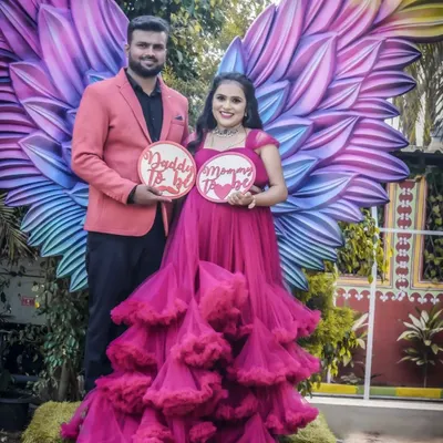 A fun and imaginative shot using the angel wings backdrop. The couple holds "Daddy To Be" and "Mommy To Be" signs, creating a playful and memorable portrait.