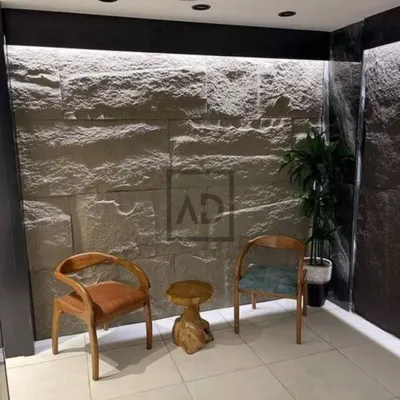 This finished accent wall in a waiting area uses PU stone panels with integrated strip lighting at the top. The light grazes the surface, highlighting the rugged texture and creating a warm, inviting atmosphere.