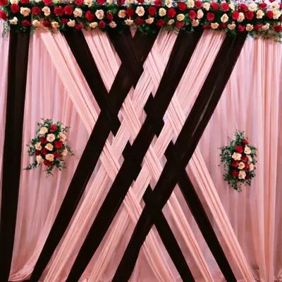This backdrop is all about texture and elegance, featuring intricately woven drapes of blush pink and rich brown fabric. The design is crowned with a lush arrangement of red and cream roses, creating a timeless and classic look for any celebration.