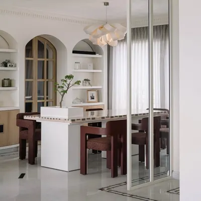 An overview of the dining area in Eden House, a lush penthouse in Bengaluru. The design combines modern lines with whimsical details, like the floral-inspired chandelier and arched shelving.