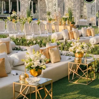 A luxurious outdoor seating lounge with pristine white sofas, intricate Moroccan-style backdrops, and elegant gold and glass tables. This setup is perfect for a chic, modern wedding.