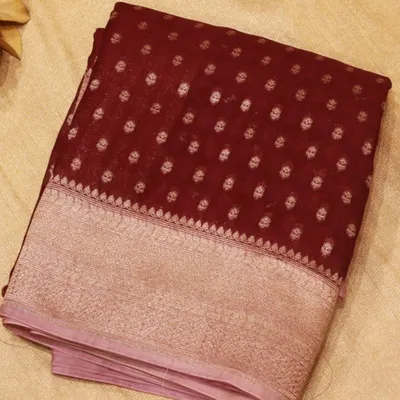 A dark maroon Kora silk saree adorned with beautiful floral motifs and a grand silver zari border. Kora silk is known for its texture and lightweight feel, offering a graceful drape.