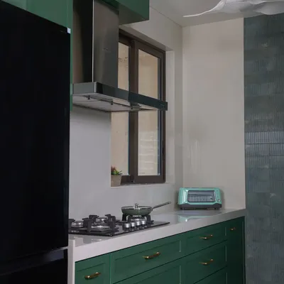 This stunning green kitchen is finished with premium quality laminate and full-body tiles. A sleek Italian marble breakfast counter seamlessly connects the kitchen and living room, serving as a stylish focal point.
