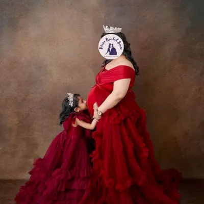 A heartwarming portrait of a mother and daughter in matching burgundy ruffled gowns. Including older siblings is a wonderful way to celebrate the new addition to your family.