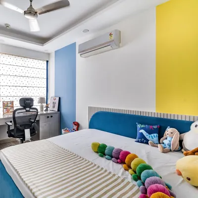 A vibrant and cheerful kid's room featuring a custom blue bed, a compact study desk, and bold color-blocked walls in yellow and blue to stimulate creativity.
