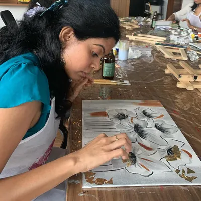 A participant carefully applies gold leaf to her floral painting. This technique adds a touch of luxury and a beautiful shimmer that makes any artwork pop.