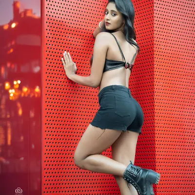 An edgy urban fashion shot using a vibrant red perforated wall as a graphic backdrop. The contrast between the red wall and the black outfit creates a bold and modern look.