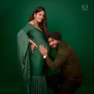 A partner lovingly listens to the baby bump in this studio shot. The mom-to-be is wearing a beautiful bottle green mermaid gown with cape sleeves, creating an intimate and stylish portrait.