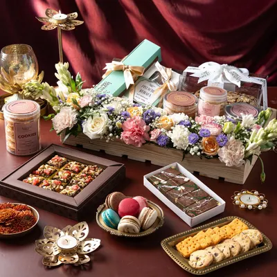 A stunning spread of my Diwali offerings, featuring a wooden crate hamper with fresh flowers, boxes of assorted cookies and macarons, and jars of treats. This showcases the variety available, from individual boxes to comprehensive gift hampers.