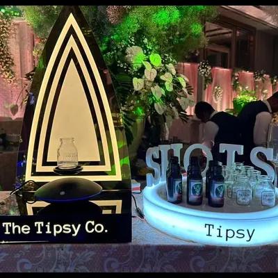 A stylish shot bar setup, perfect for an anniversary party in Kolkata. The illuminated "Tipsy" sign and custom bottle glorifier add a modern, celebratory touch.