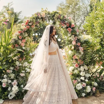 A bride stands gracefully before a lush floral archway, creating a perfect photo opportunity and a beautiful entrance to the ceremony.