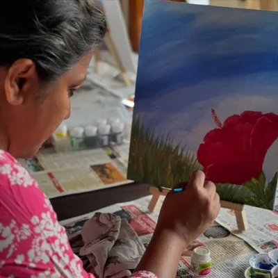 A participant lost in the moment, adding the final touches to her painting of a red hibiscus flower.