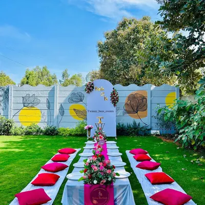 A beautiful outdoor picnic-style setup for a "Bride to be" party. We arranged a low table with a floral runner and comfortable floor seating on a lush green lawn for a relaxed and stylish celebration.