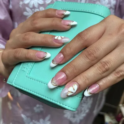 A close-up of custom nail extensions, featuring an elegant French manicure enhanced with a delicate gold chrome outline and handcrafted 3D floral art. This is the kind of detailed, glamorous look I love to create.