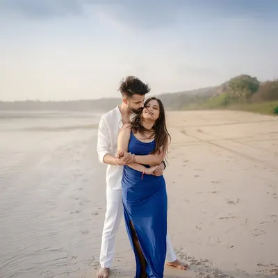 A gentle embrace on the sand, with the soft light of the setting sun creating a warm glow. This is a classic romantic beach portrait, focusing on the connection and tenderness between the couple.