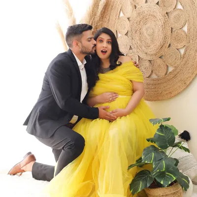 A playful and candid moment captured during a maternity session. The bright yellow gown and bohemian-style backdrop create a cheerful and sunny atmosphere, perfect for celebrating this happy time.