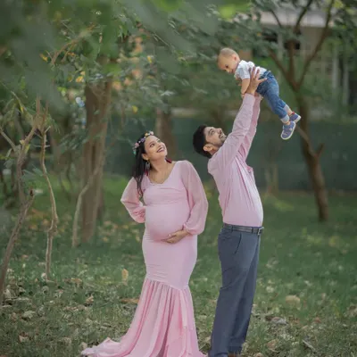 This photo perfectly captures a family in transition. The parents' joy, the toddler's excitement, and the visible baby bump tell a complete story of a growing family.