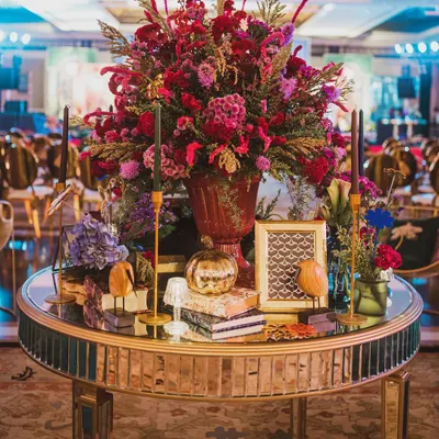 A stunning centerpiece for a contemporary sangeet. I love combining lush florals with unique decorative objects like this mirrored table, patterned books, and a golden pumpkin.